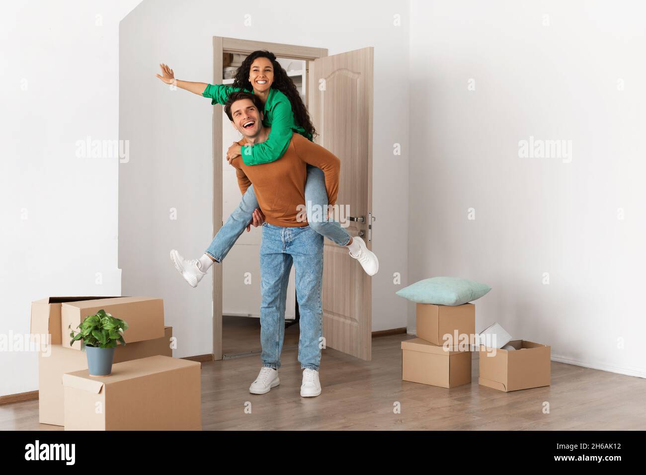 Festeggiamo il giorno del movimento. Coppia felice festeggia il trasferimento a casa propria, ragazzo allegro dando la signora piggyback corsa, eccitato giovane famiglia millennial Foto Stock