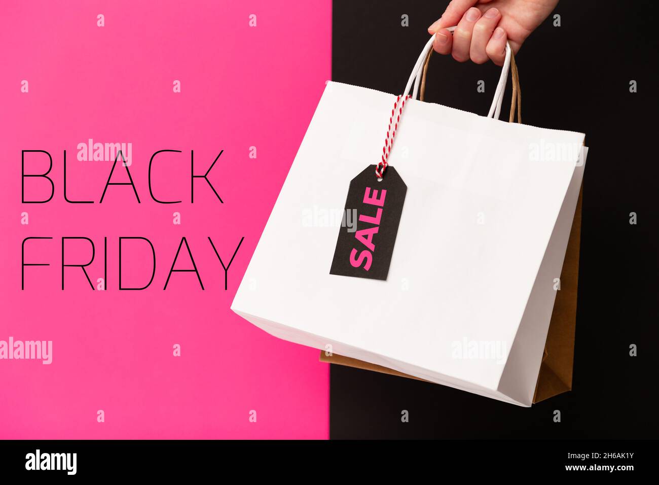 Black Friday, mano femminile che tiene due borse shopping con vendita tag prezzo isolato su sfondo rosa e nero. Offerta black friday, sconto, shopping c Foto Stock