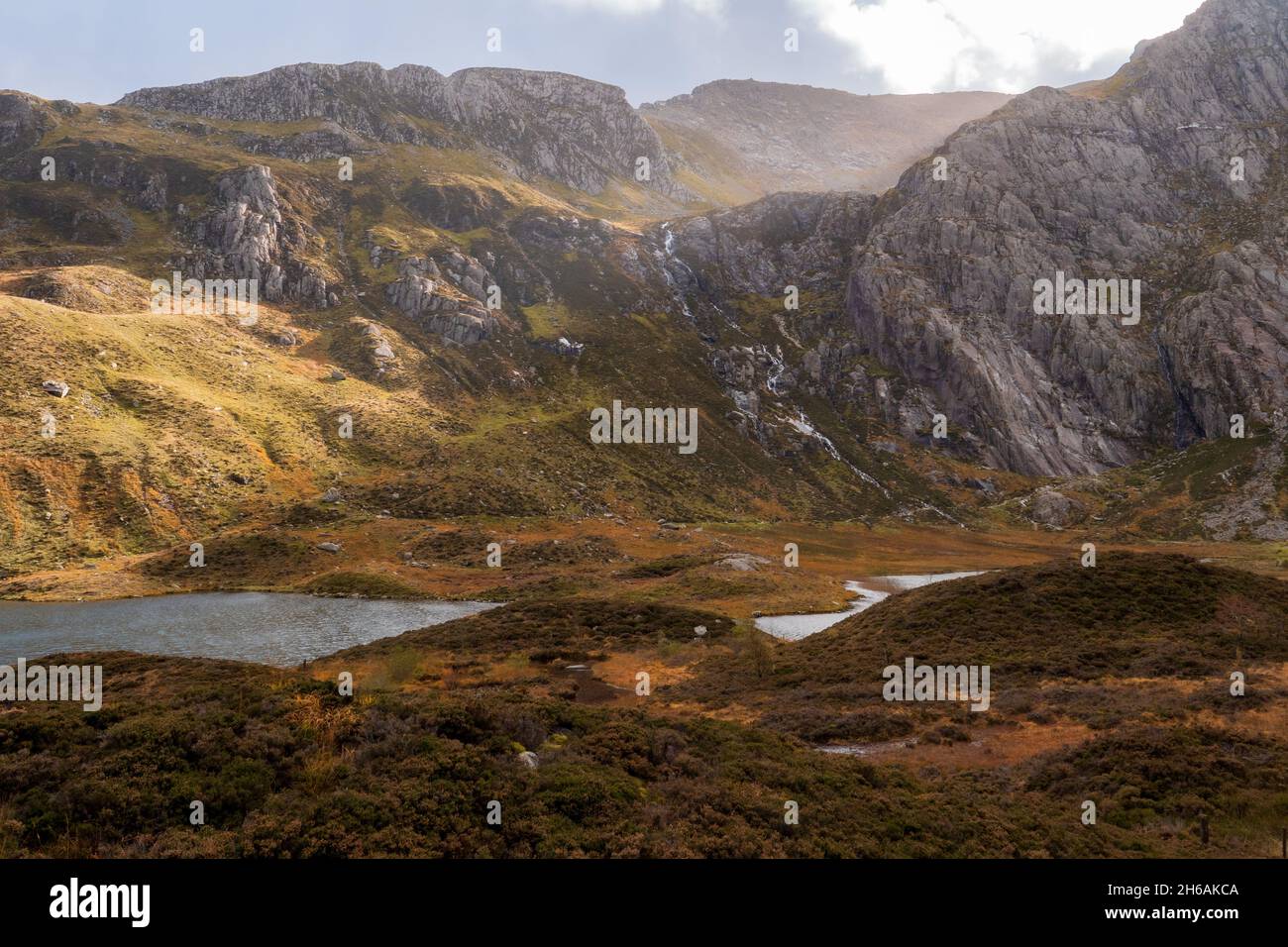 La luce del sole che si infrangono attraverso le nuvole su una montagna in autunno sopra un lago a Snowdonia, Galles Foto Stock