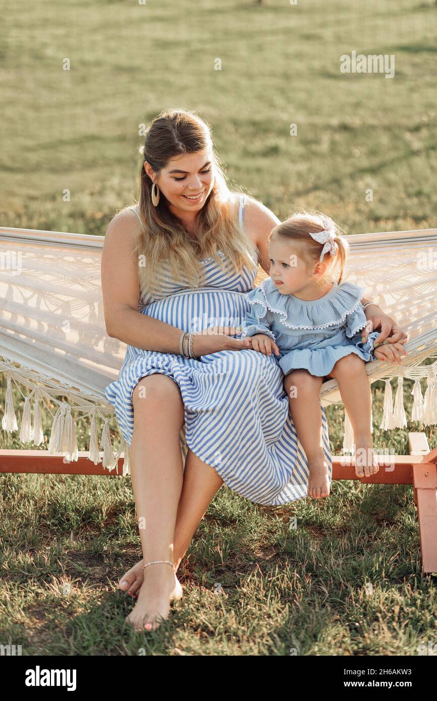 Affascinante donna incinta in estate la sundress sta riposando con la sua figlia piccola in amaca in natura, bambino di 3 anni. Materiali naturali. Buon ch Foto Stock