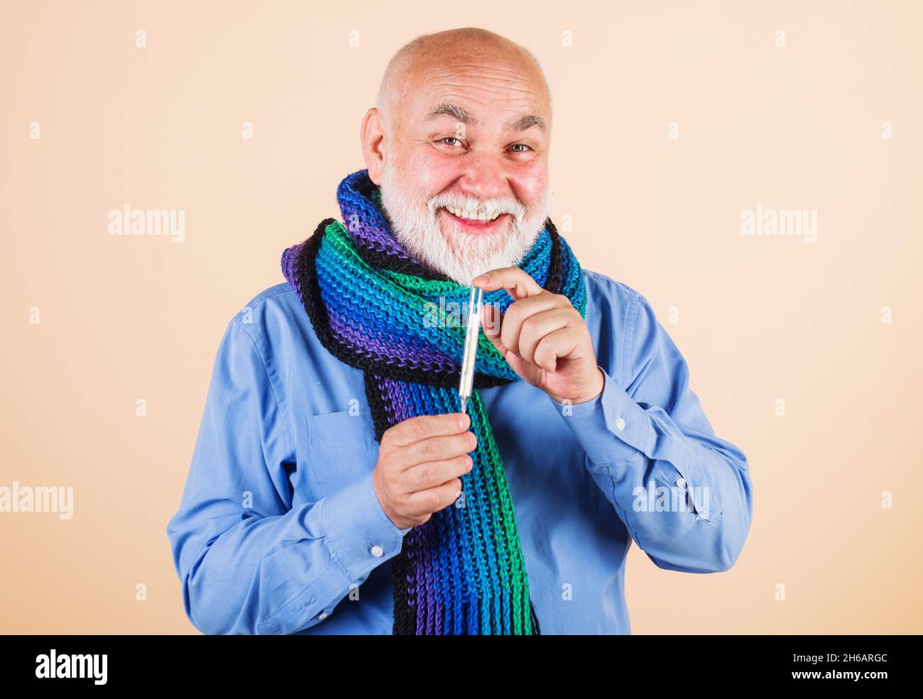 Uomo sorridente in sciarpa con termometro. Medicina, trattamenti e concetto di assistenza sanitaria. Foto Stock