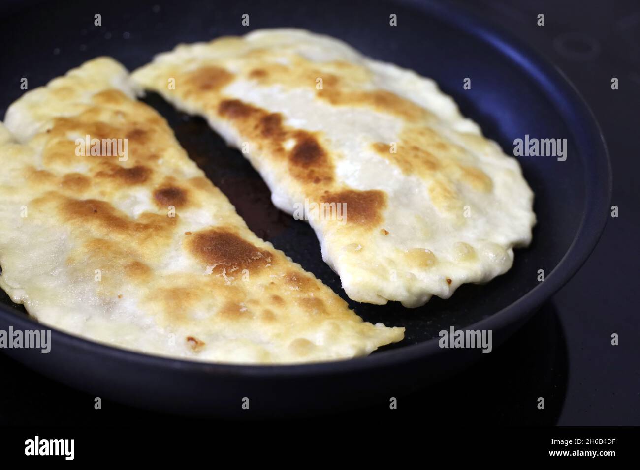 Friggere gli scudetti su una stufa elettrica a induzione, piatto orientale tradizionale. Tortilla fatta in casa con carne su padella nera fritta in olio Foto Stock