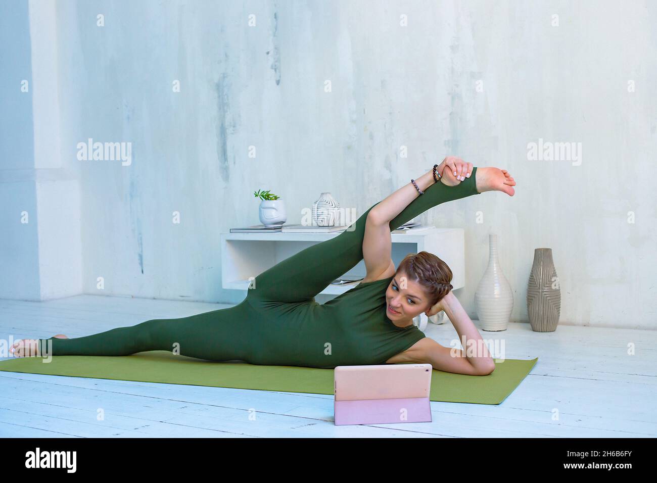 Donna bella e snella in abbigliamento sportivo verde pratica yoga online  utilizzando un tablet digitale in interni bianchi Foto stock - Alamy