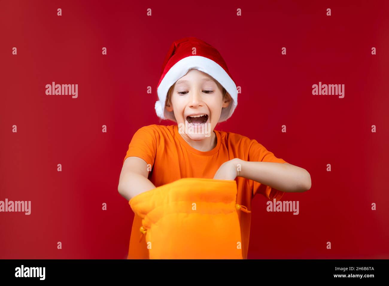 Un ragazzo in un cappello di Santa rummages in un sacchetto giallo del regalo di Natale e ride ad alta voce Foto Stock