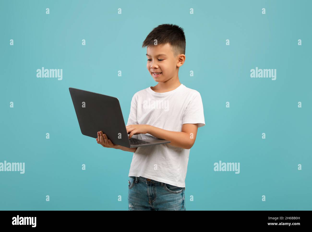 Ritratto di piccolo ragazzo asiatico utilizzando laptop mentre si sta in piedi su sfondo blu studio, cheerful coreano Kid maschio digitando sul computer, Studio on-line o Pla Foto Stock