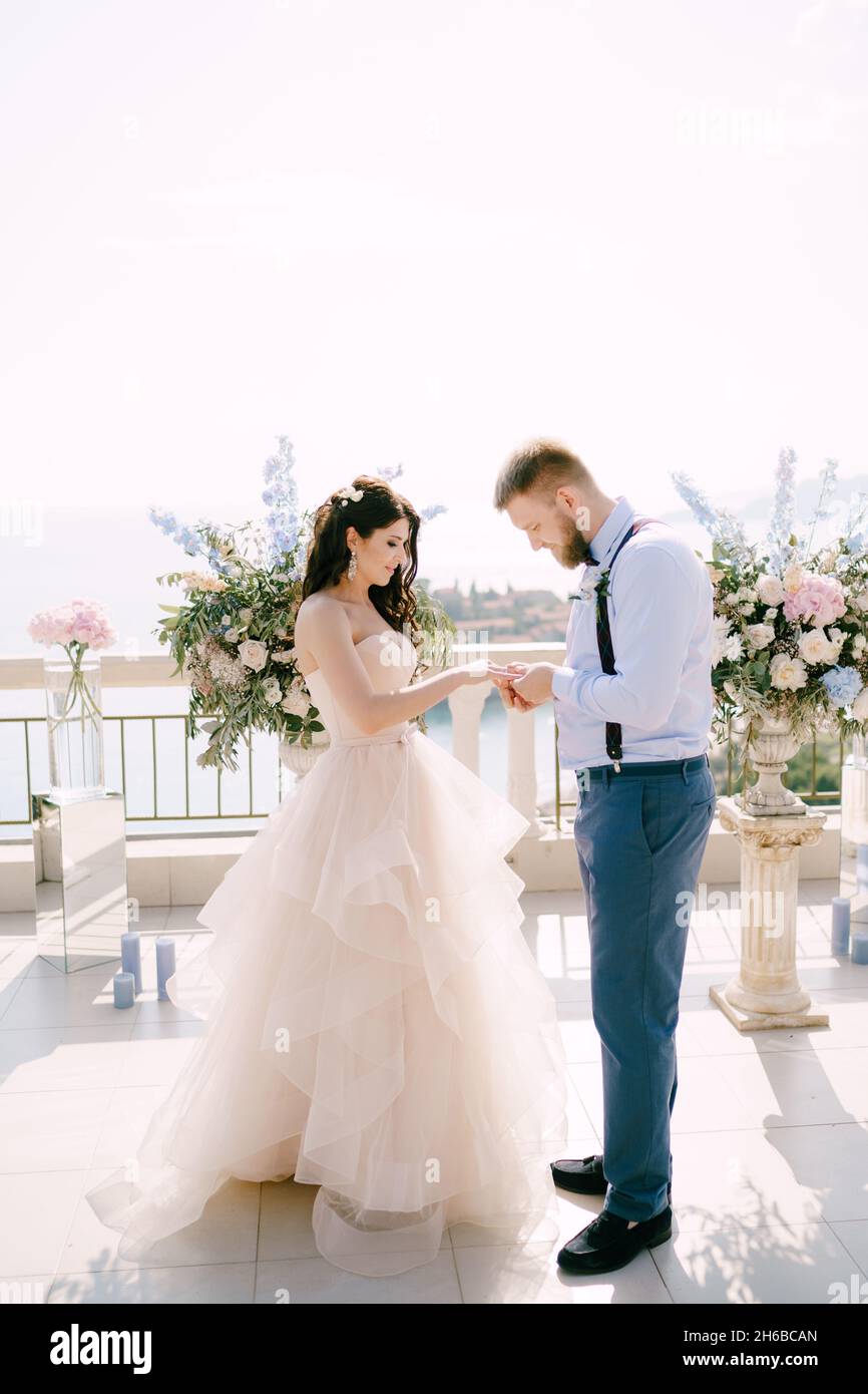 Lo sposo mette l'anello sul dito della sposa durante la cerimonia nuziale sullo sfondo delle decorazioni di nozze Foto Stock