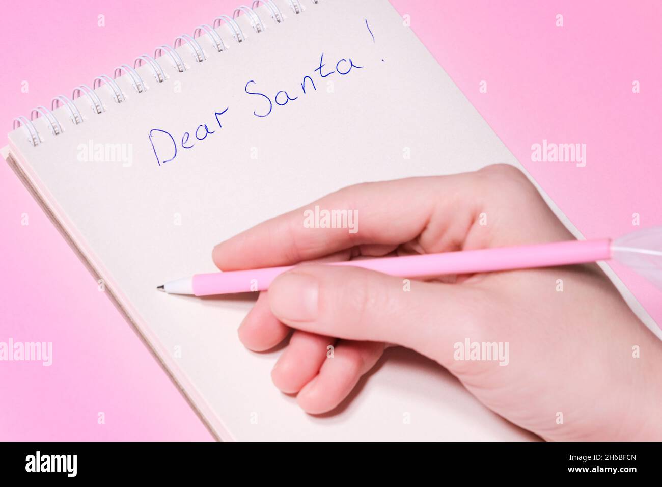 Gentile concetto di lettera di Santa. Penna rosa a mano decorata con piuma e scrittura in blocco note lettera a Babbo Natale su sfondo rosa. Foto Stock
