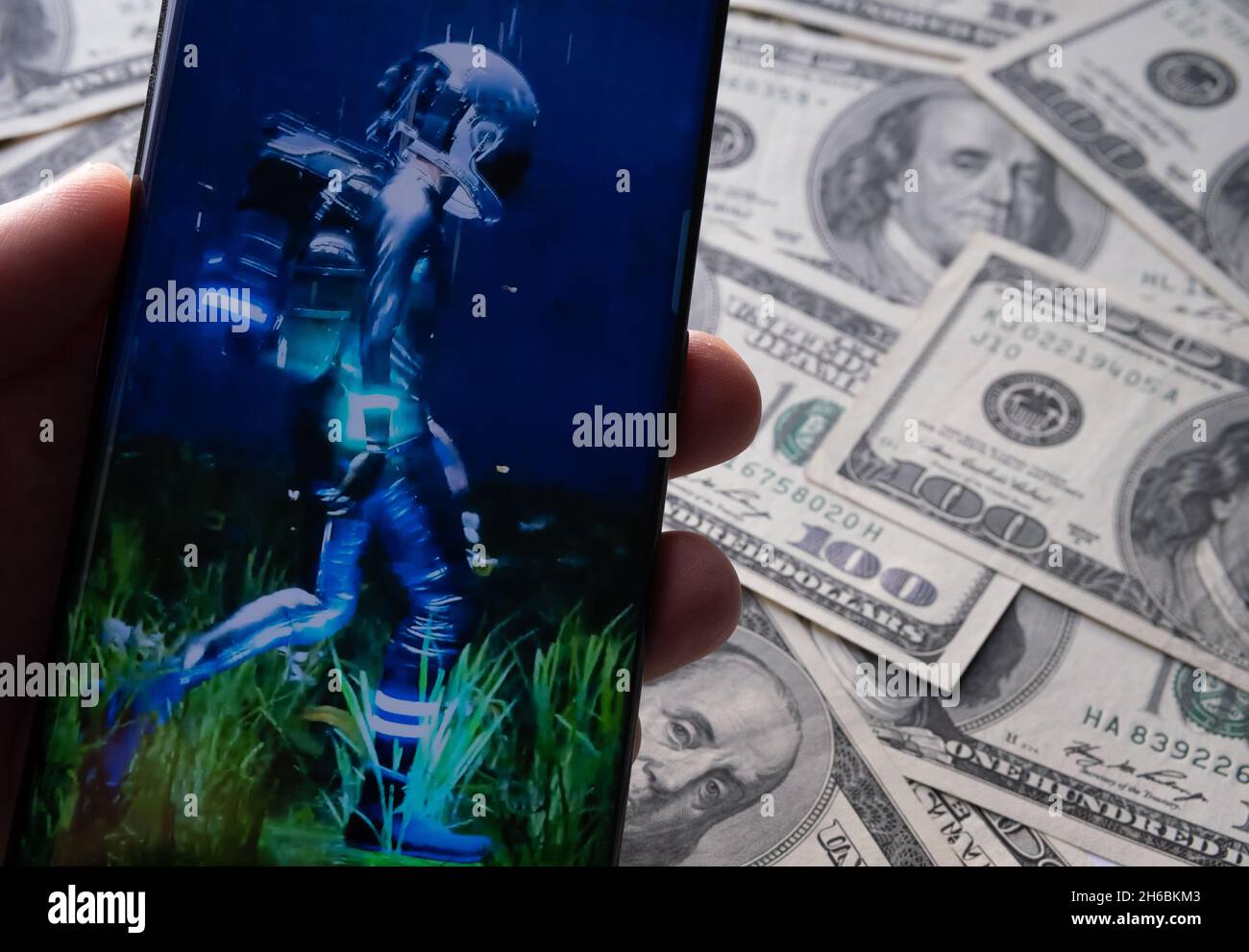 L'immagine del fotogramma NFT "UMANO" di Beeple è visibile sullo smartphone e sulle bollette del dollaro sullo sfondo sfocato. Stafford, Regno Unito, 14 novembre 2021. Foto Stock