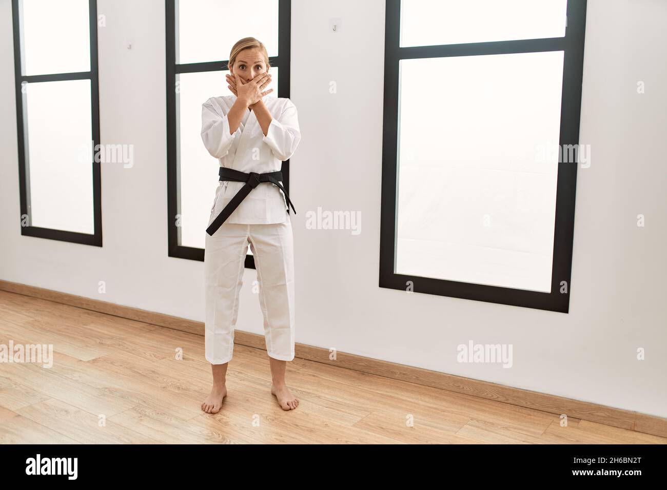Giovane bionda caucasica che indossa karate kimono e cintura nera scioccata  coprendo la bocca con le mani per errore. Concetto segreto Foto stock -  Alamy
