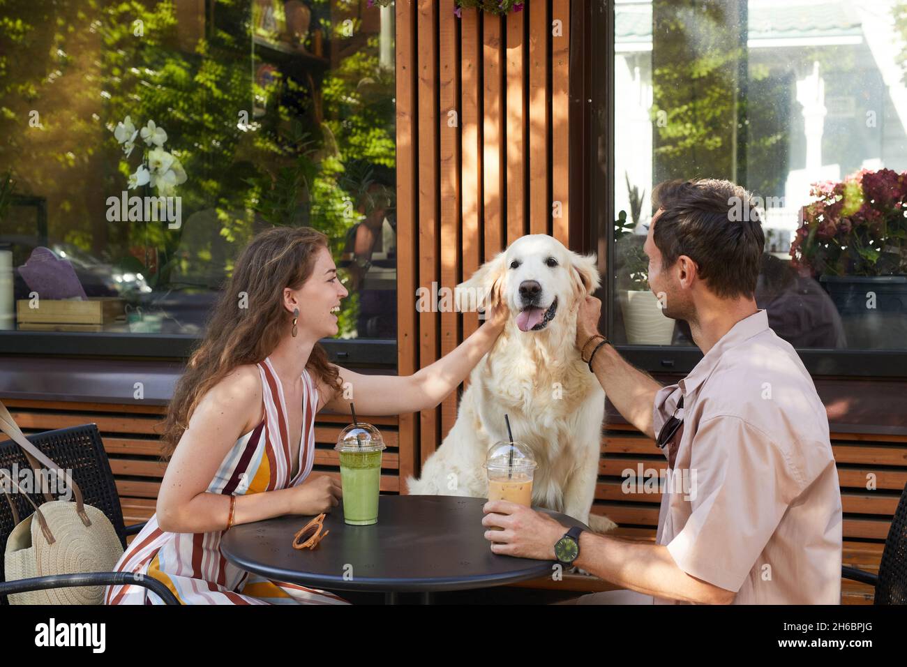 Ritratto di coppia felice con cane seduto a tavola insieme in un bar all'aperto e ridendo, spazio copia Foto Stock
