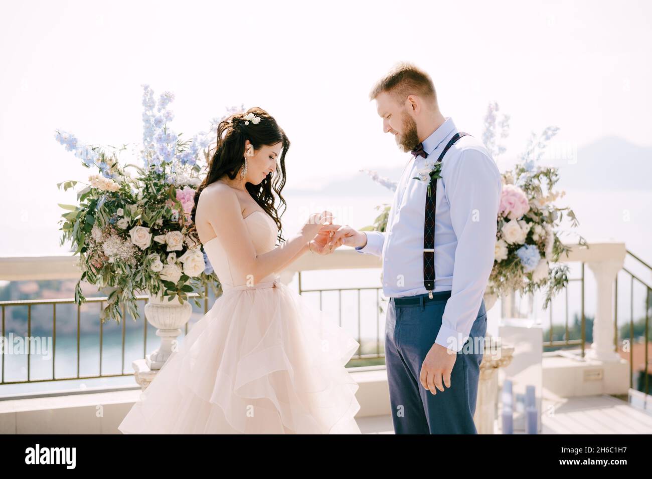 La sposa mette lo sposo sul dito della sposa durante la cerimonia nuziale sullo sfondo delle decorazioni di nozze Foto Stock