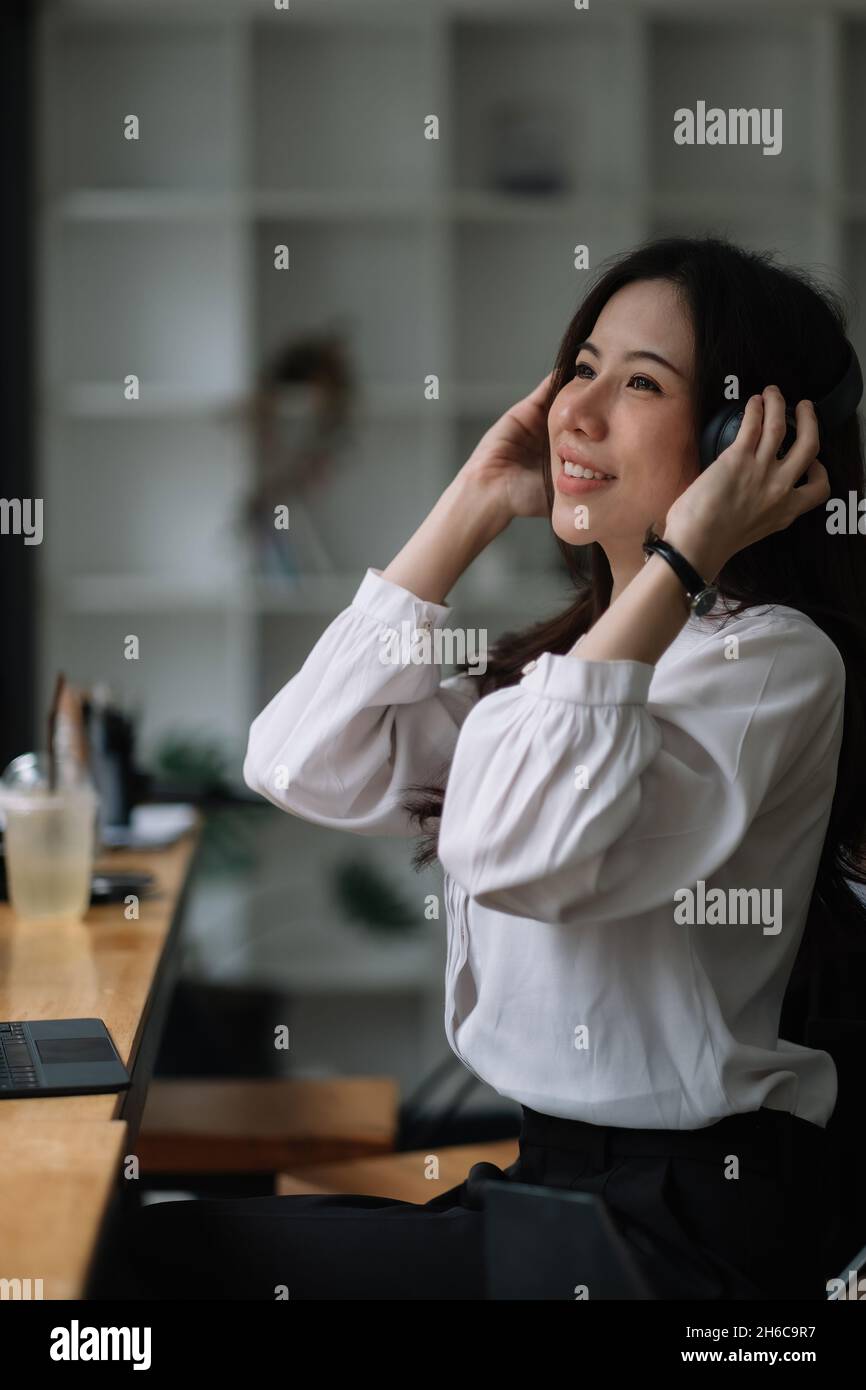 Ritratto bella ragazza asiatica ascoltare la musica con cuffie e leggere libri mentre si siede al tavolo nella caffetteria Foto Stock