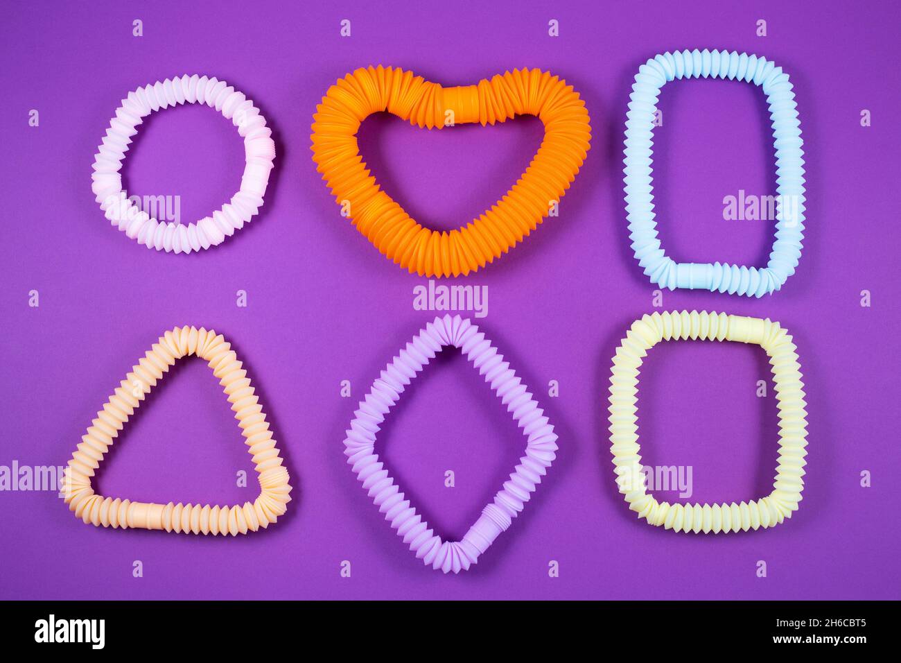 Tubi pop colorati sotto forma di figure geometriche su sfondo viola. Giocattoli antistress per le dita per adulti e bambini. Foto Stock