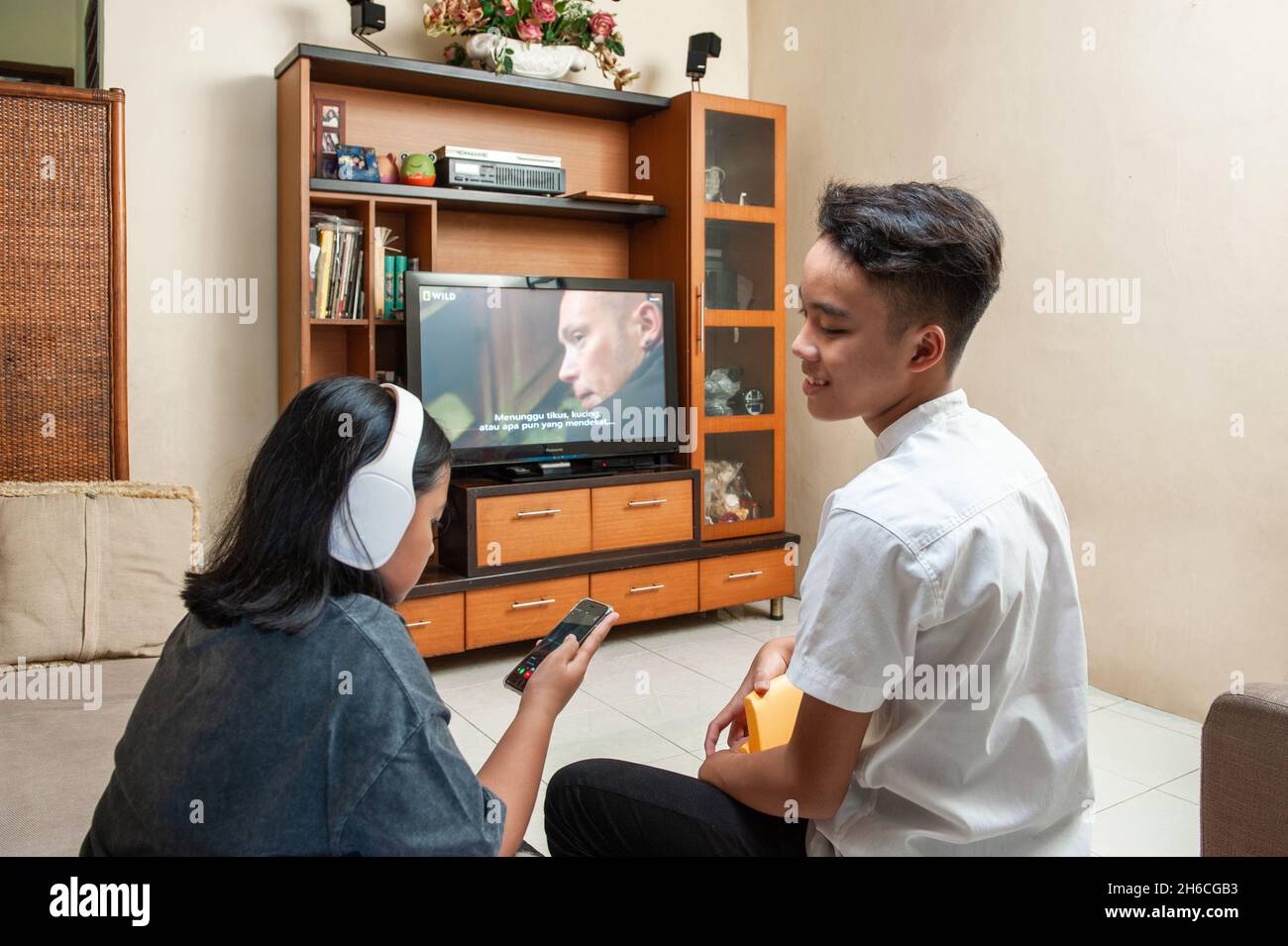 Giovane maschio indonesiano che guarda la tv e la sorella che ascolta musica Foto Stock