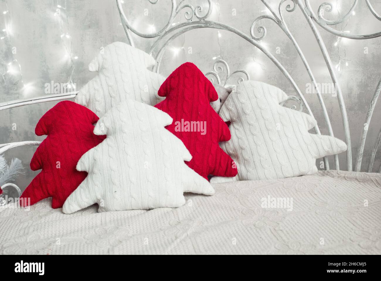 Cuscini decorativi di Natale sul letto. Cuscini bianchi e rossi in maglia a forma di pino su divano con luci Foto Stock