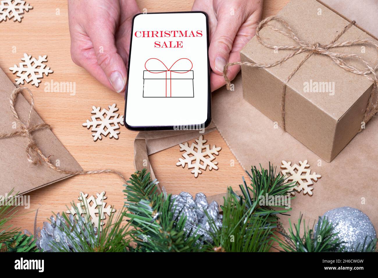 Vendita online di Natale. Primo piano le mani tenendo un telefono cellulare con uno schermo bianco con la vendita iscrizione e un regalo su un tavolo di legno con Natale Foto Stock