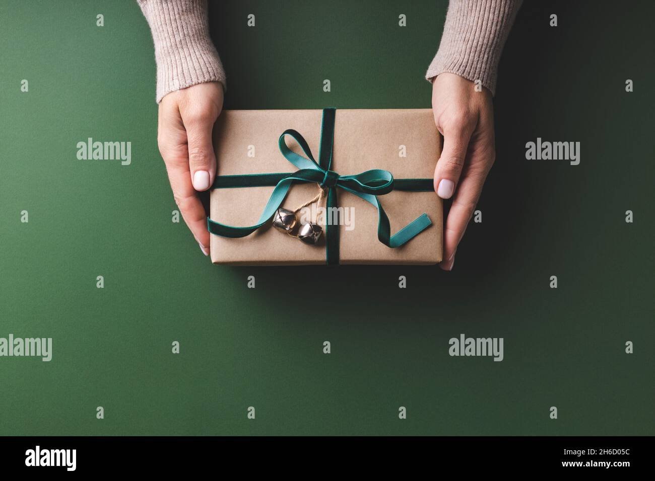 Le mani femminili che tengono la scatola del regalo di Natale nastro di velluto legato su sfondo verde. Foto Stock