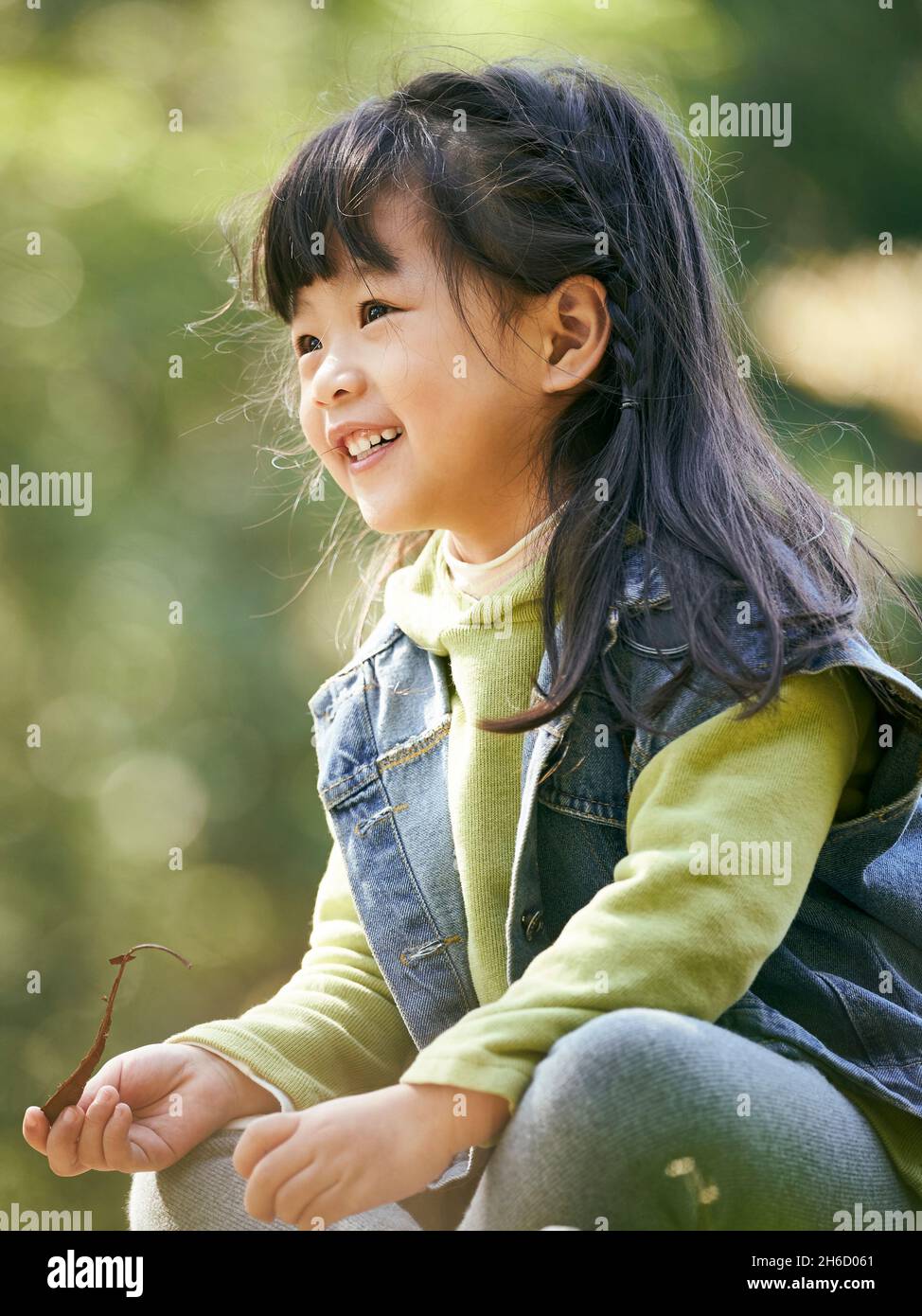 ritratto all'aperto di una bambina asiatica seduta su erba felice e sorridente Foto Stock