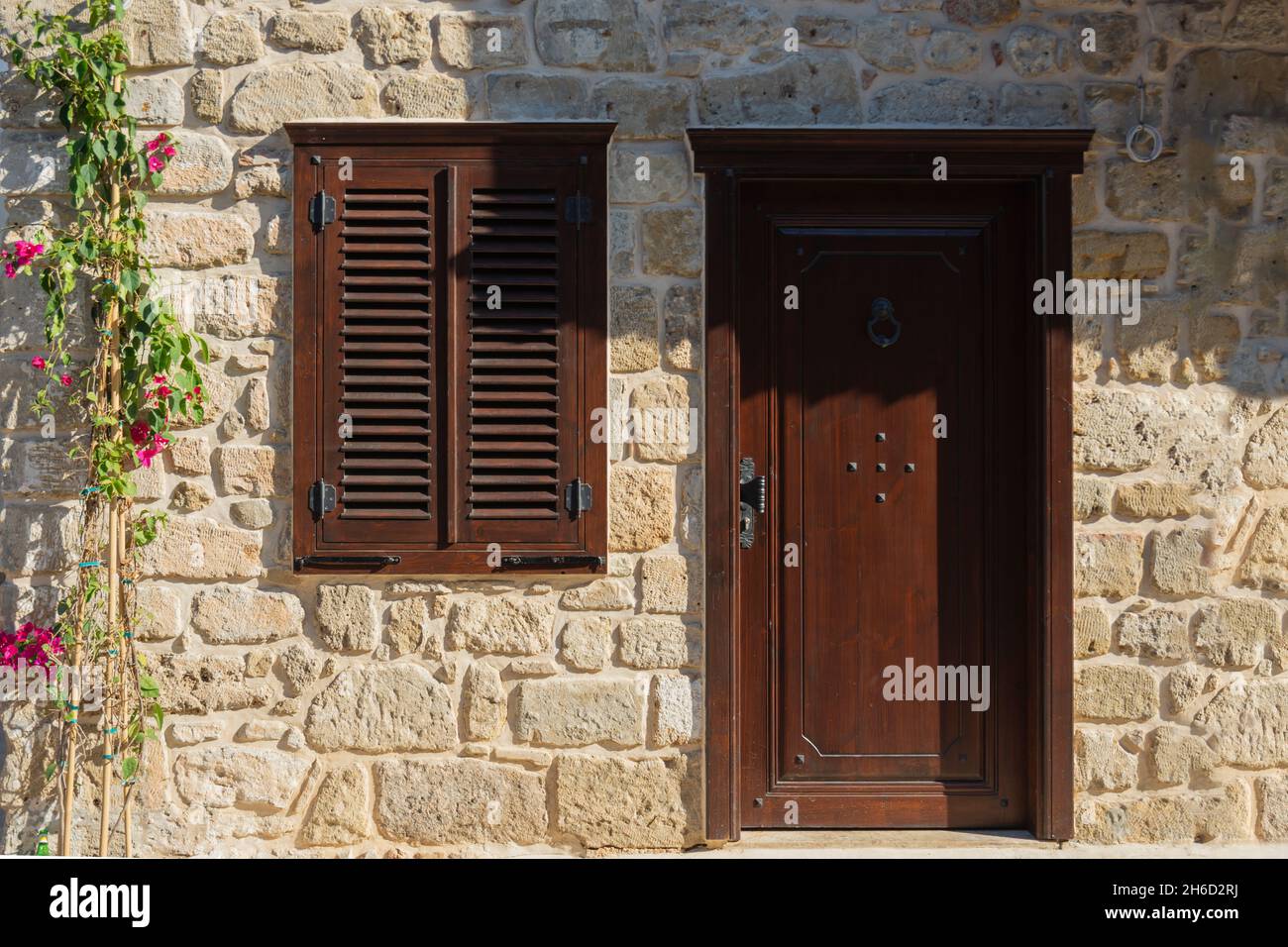 Casa con persiane marrone e porta in Antalya Side Village.Seective Focus. Muro di pietra e fiore di edera. Foto Stock