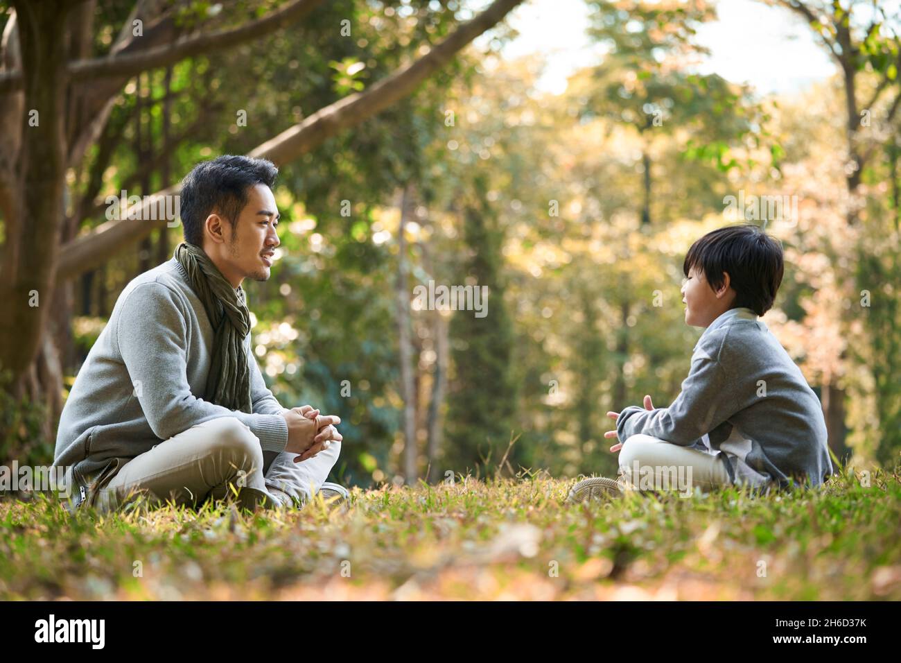 padre e figlio asiatici seduti sull'erba per una piacevole conversazione all'aperto nel parco Foto Stock