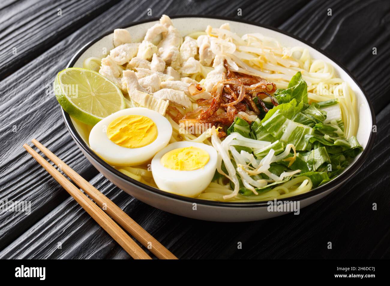 Soto Ayam è una classica zuppa di pollo indonesiana ma anche popolare a Singapore e Malesia primo piano sul piatto sul tavolo. Orizzontale Foto Stock