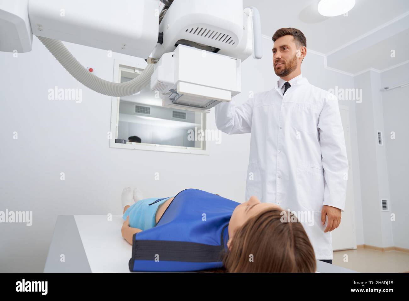 Radiologo professionista premere i pulsanti utilizzando il moderno strumento a ultrasuoni per donna in accappatoio blu sicuro. La donna si sdraia giù lo stomaco di scansione su procedura di ecografia in clinica. Foto Stock