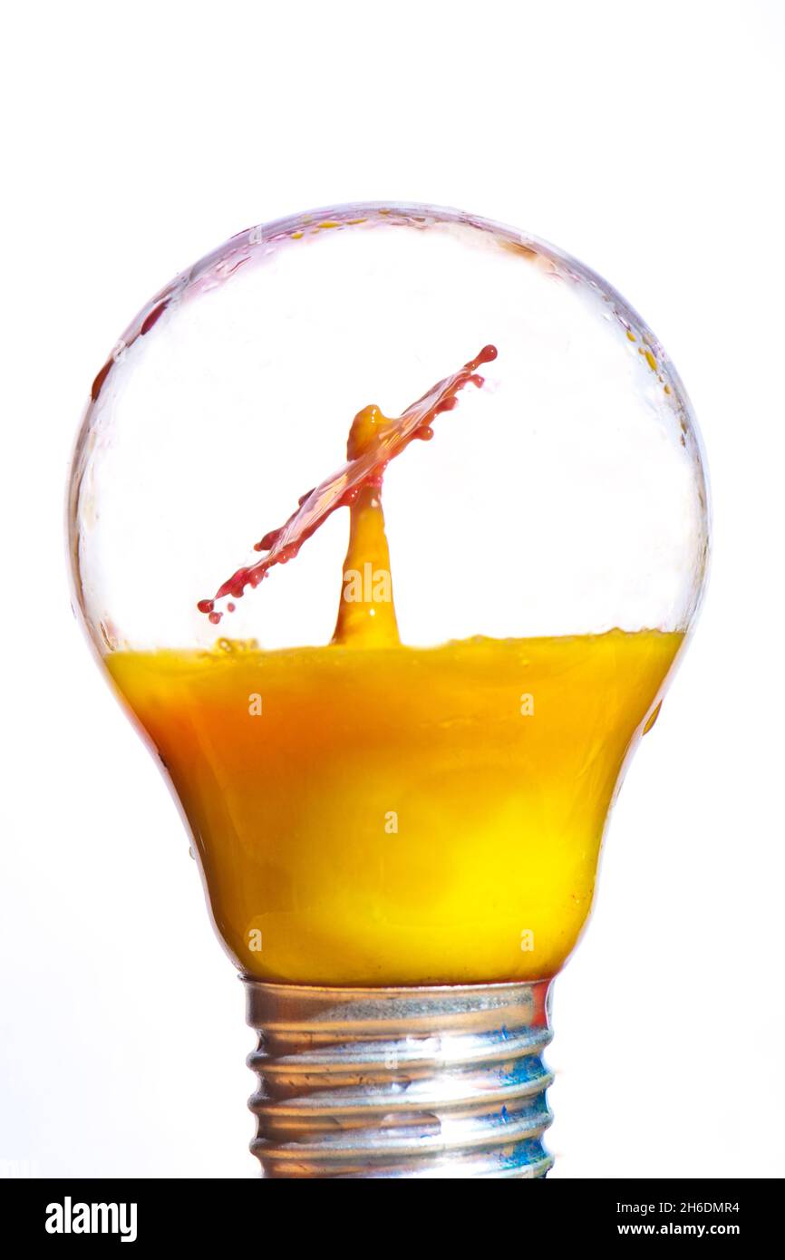 Gocce di liquido fotografico flash ad alta velocità (succo d'arancia) all'interno di una lampadina sigillata. Foto Stock