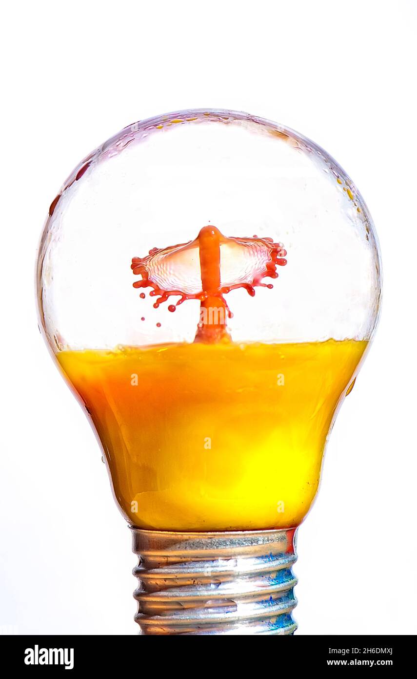 Gocce di liquido fotografico flash ad alta velocità (succo d'arancia) all'interno di una lampadina sigillata. Foto Stock