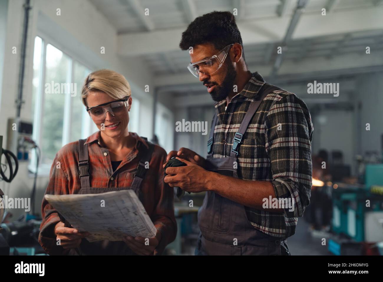 Ritratto di giovani colleghi industriali biraciali che lavorano in ambienti interni in un laboratorio di metallo, sorridendo. Foto Stock