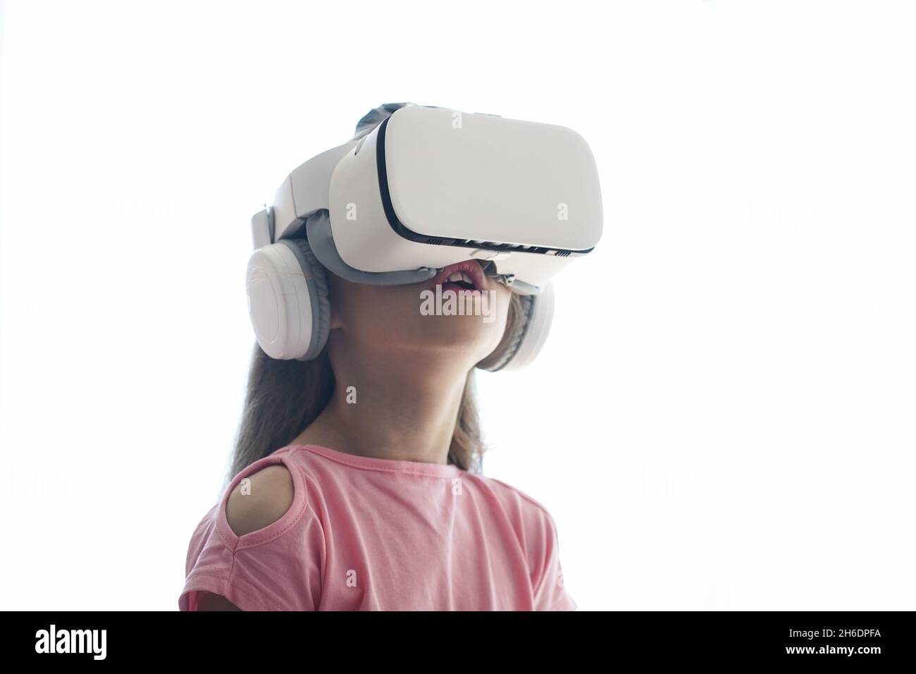 La ragazza si sta divertendo in occhiali di realtà virtuale, in piedi su uno sfondo bianco. Spazio di copia. Foto di alta qualità Foto Stock