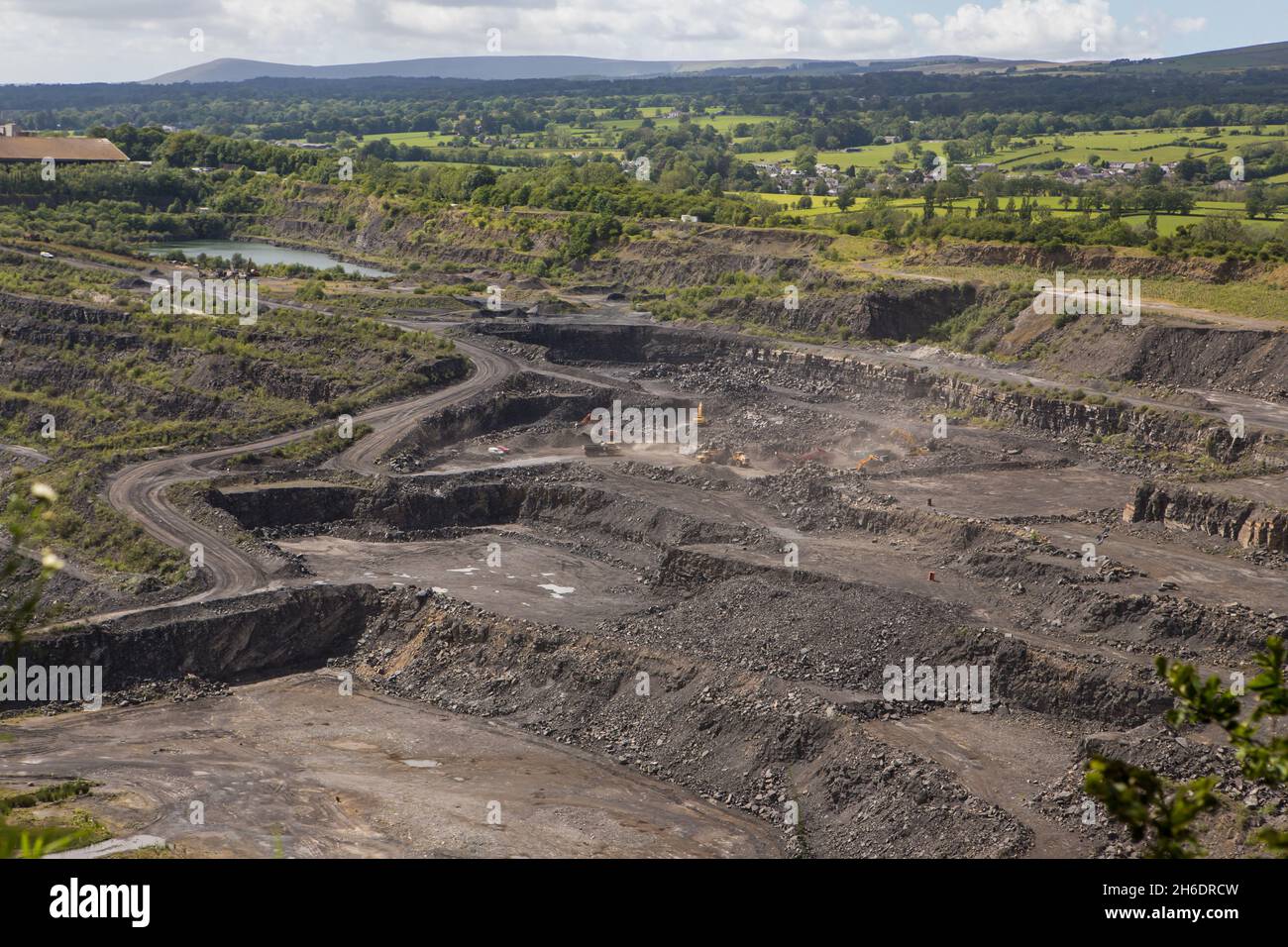 Grande cava di pietra calcarea a Clitheroe, Ribble Valley. Escavatori e camion che lavorano con terrazze di roccia sulle pareti della cava Foto Stock