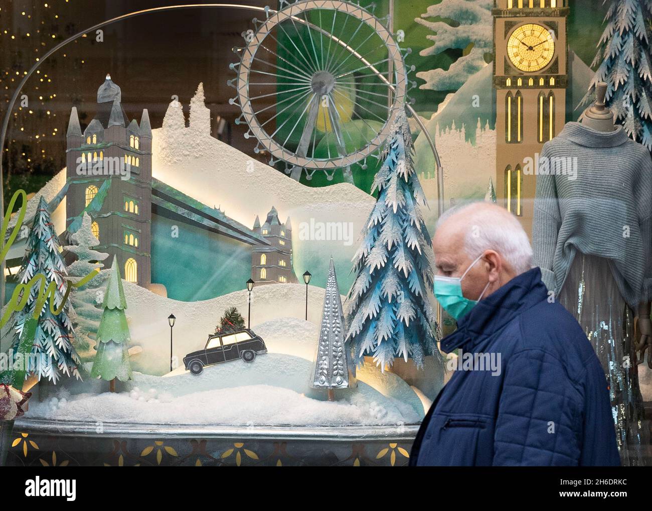 Le persone che indossano le maschere protettive Covid-19 passano davanti a una vetrina a tema natalizio su Regents Street, Londra. Foto Stock