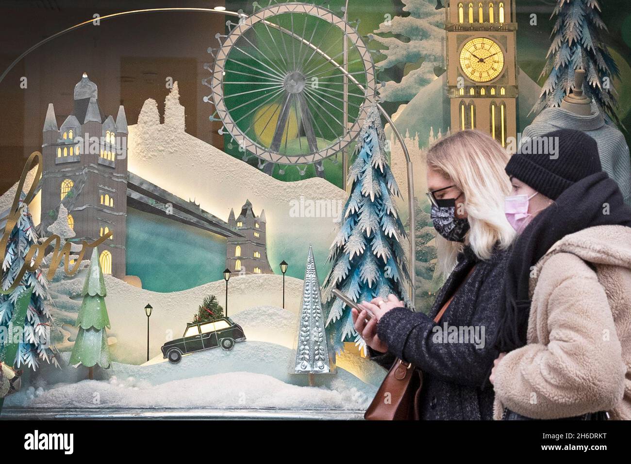 Le persone che indossano le maschere protettive Covid-19 passano davanti a una vetrina a tema natalizio su Regents Street, Londra. Foto Stock