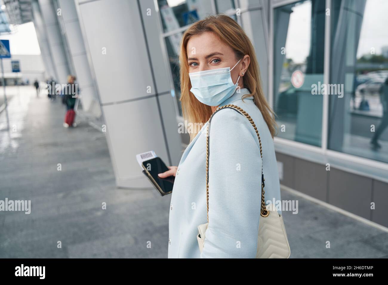 Viaggiatore aereo con biglietto d'imbarco in piedi presso l'edificio del terminal dell'aeroporto Foto Stock