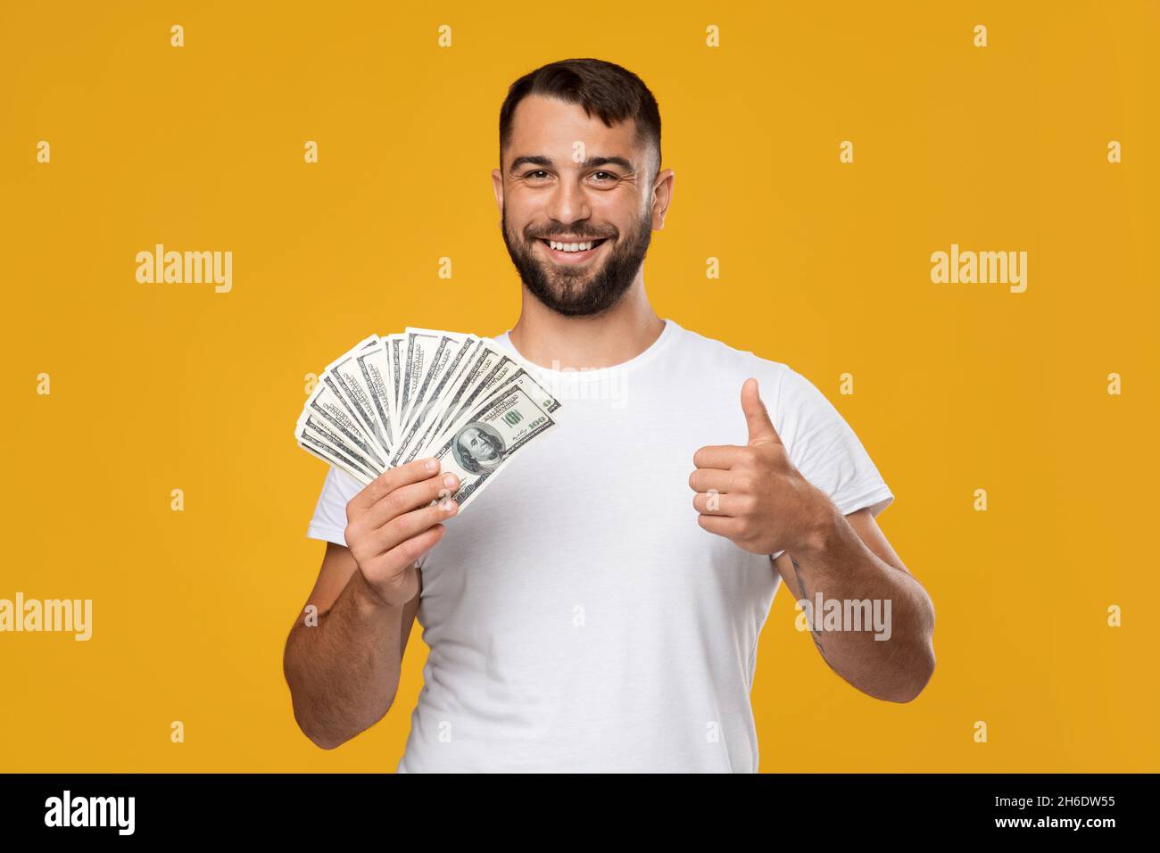 Sorridendo eccitato maschio caucasico maturo gioisce alla vittoria, tenga i soldi molto mostrano pollice in su Foto Stock
