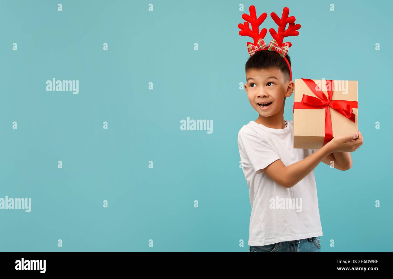 Annuncio di Natale. Divertente Little Asian Boy Holding Present Box e guardando da parte Foto Stock