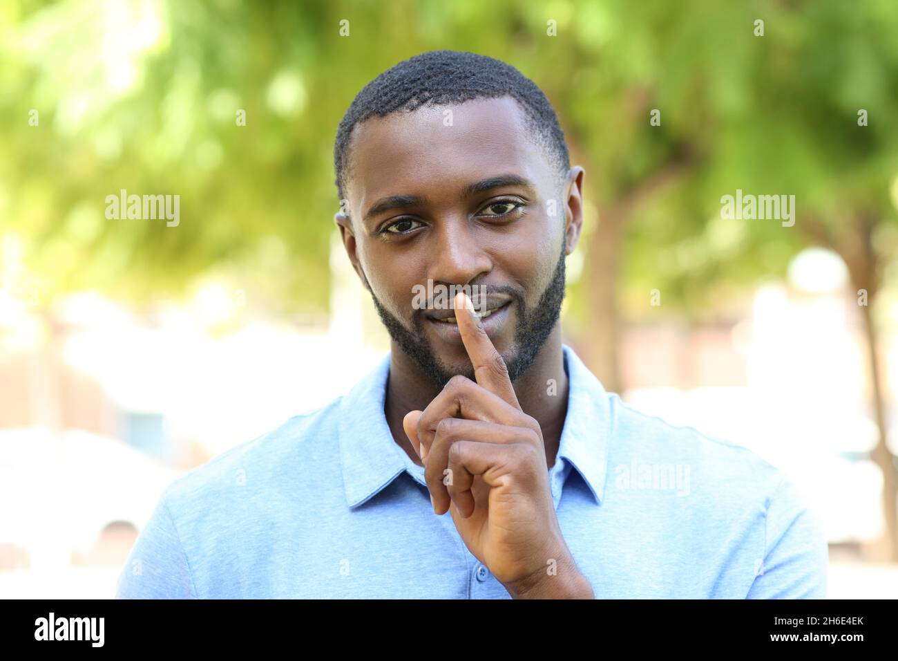 Uomo felice con la pelle nera che chiede il silenzio gesturing con l'indice in un parco Foto Stock