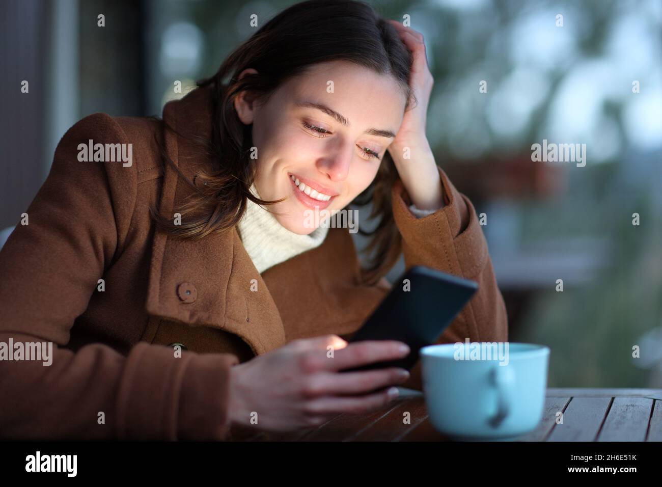 Donna felice che controlla il contenuto dello smartphone in inverno seduto in una terrazza Foto Stock