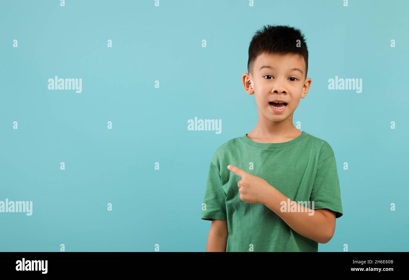 Eccitato piccolo ragazzo asiatico che punta da parte a Copy Space su sfondo blu Foto Stock
