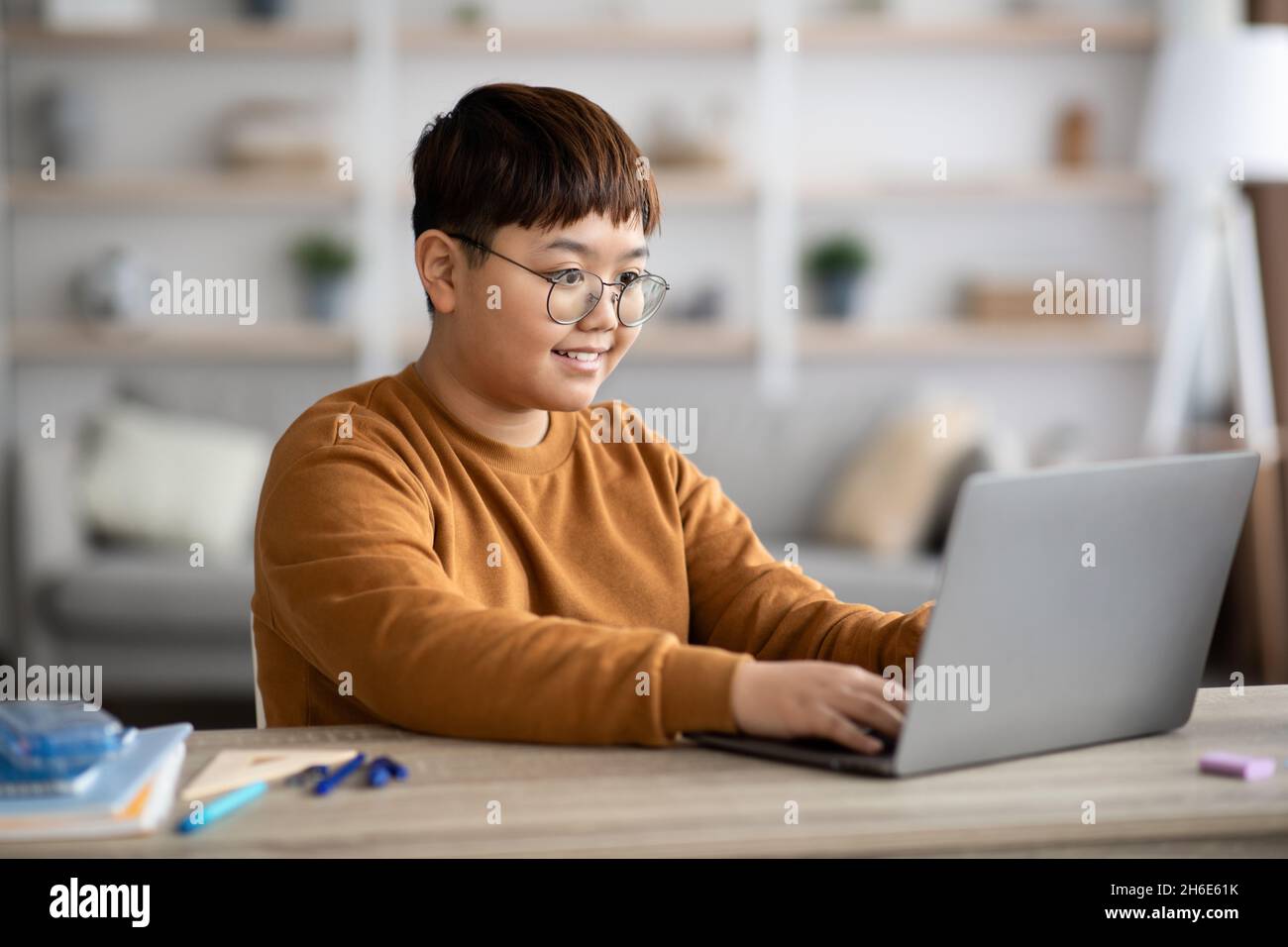 Ragazzo asiatico intelligente seduto di fronte al portatile, facendo i compiti Foto Stock