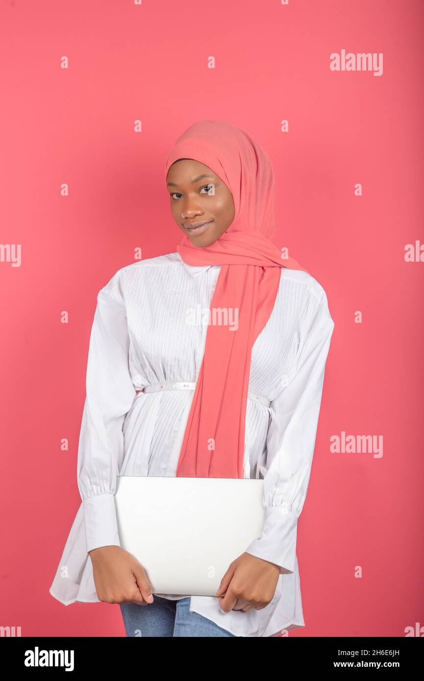 Immagine di una donna afroamericana che indossa una sciarpa rosa e tiene un laptop isolato su sfondo rosa Foto Stock