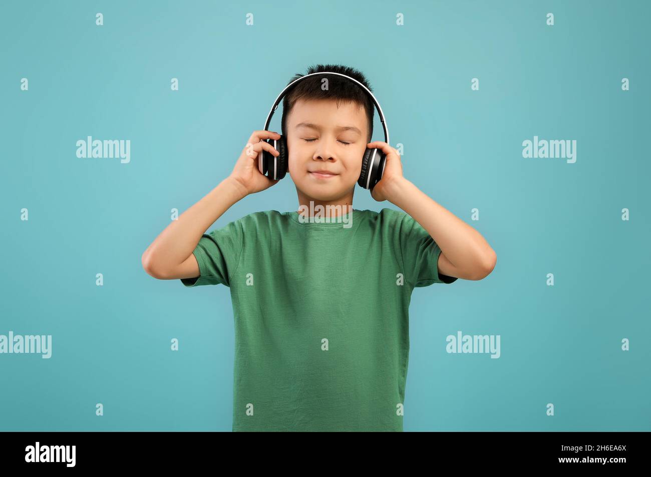 Cute Little Asian Boy indossando cuffie wireless ascoltare musica con occhi chiusi Foto Stock