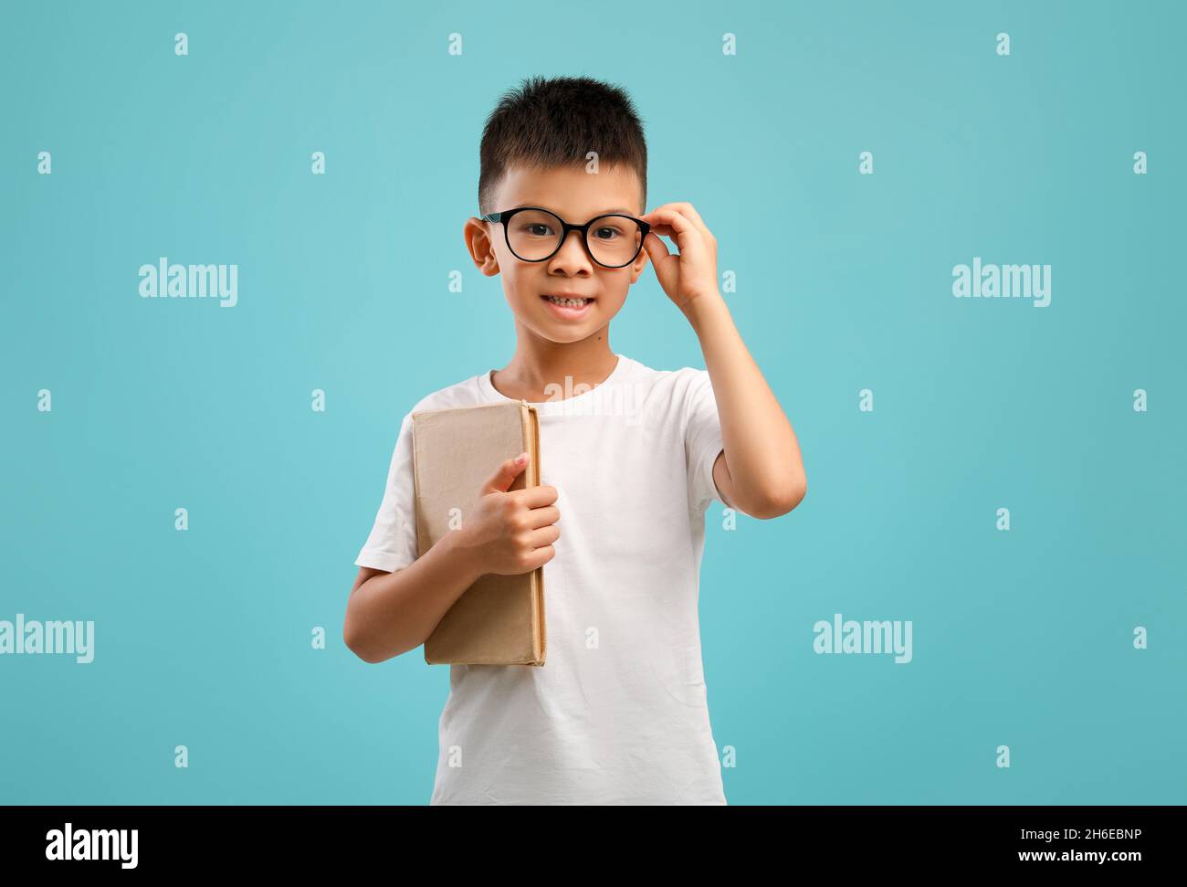 Ritratto di piccolo scolaro asiatico in occhiali con libro in mano Foto Stock