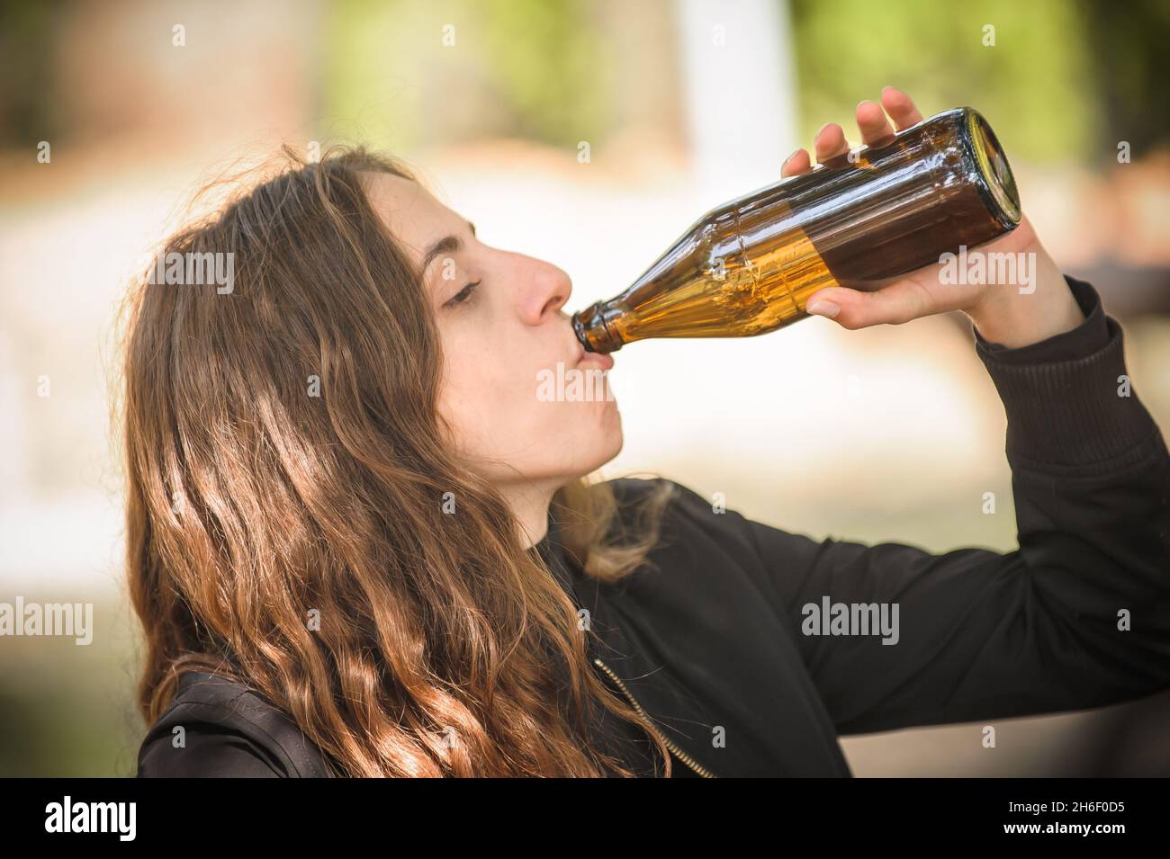 Ragazza bug birra da bottiglia su panca di legno con tavolo nel parco  forestale all'aperto. Espresso bere e veloce ottenere ubriaco stile di vita  concetto. Scena della vita reale Foto stock -