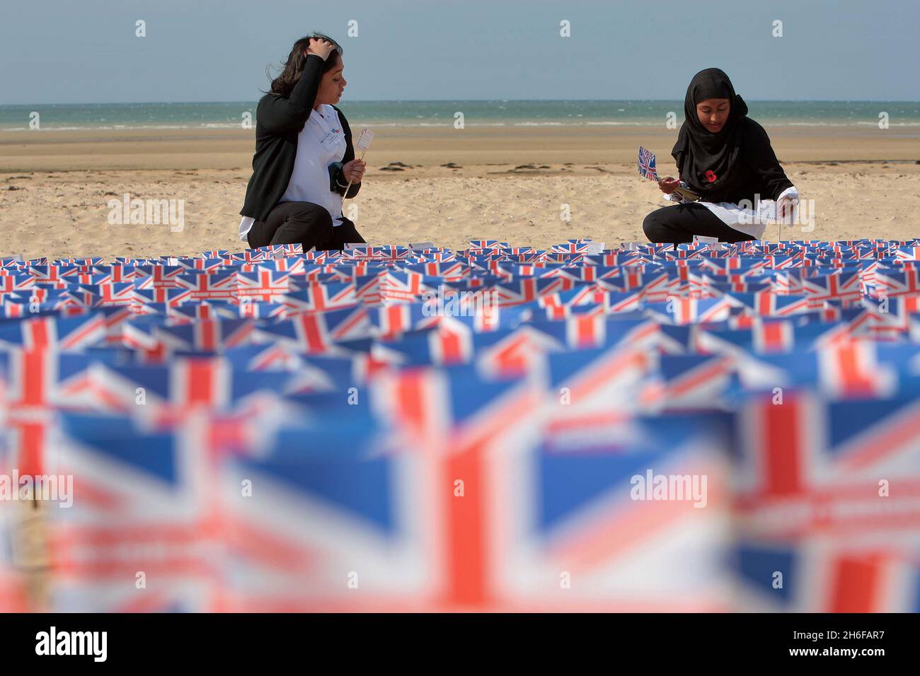 Le studentesse Fateha Chowdhury (14 anni) e Tasmina Hussain (15 anni) della Morpeth School di Bethnal Green, Londra, piazzando bandiere con centinaia di altri Union Jack Flags recanti messaggi dal pubblico britannico, hanno messo su Gold Beach ad Asnelles, Francia oggi, per ricordare coloro che hanno perso la vita nella seconda Guerra Mondiale. Foto Stock