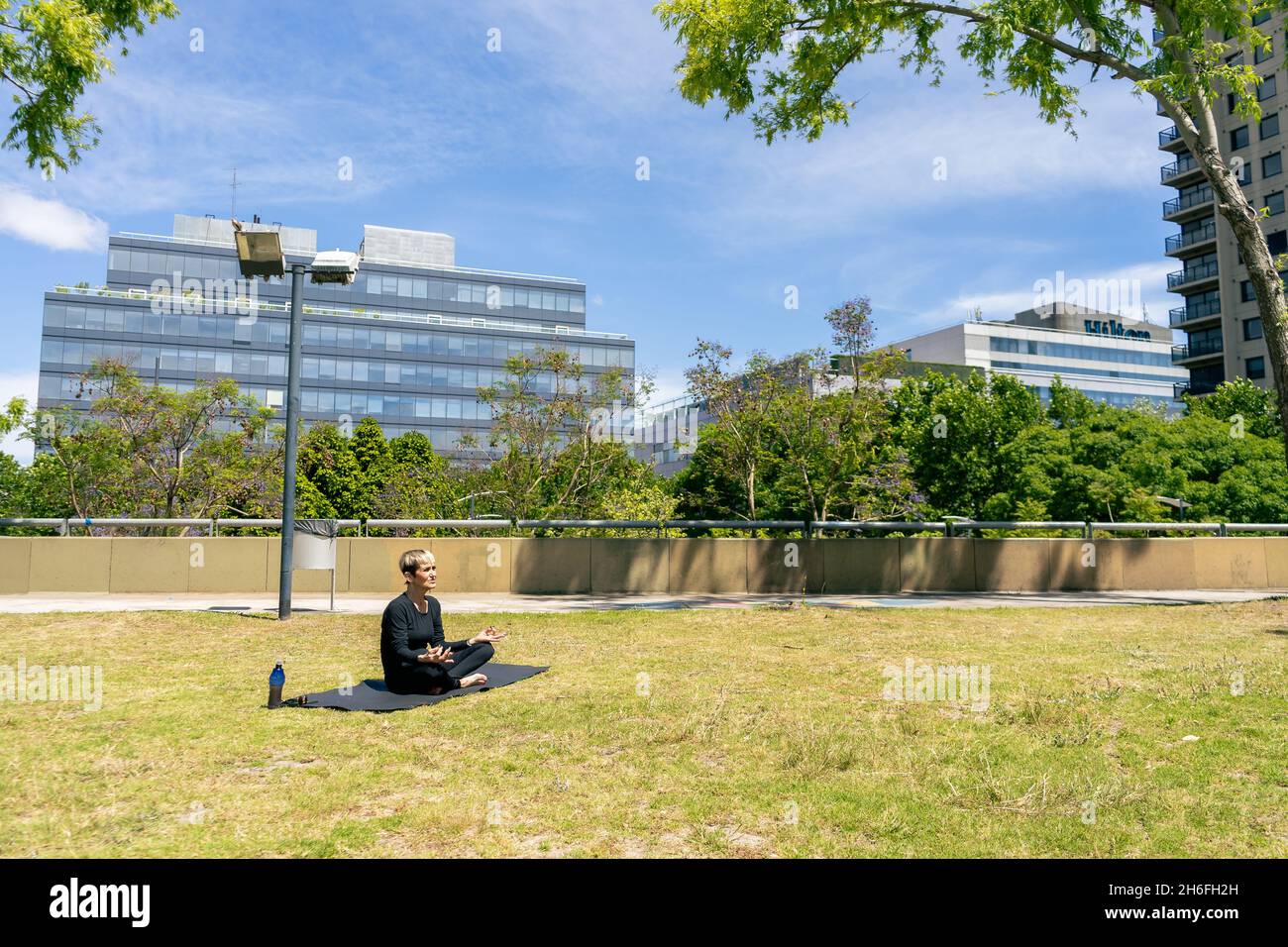 Donna matura seduta in lotus posizione pratica yoga in un parco pubblico in una giornata di sole. Concetto di vita sana, spazio copia. Foto Stock
