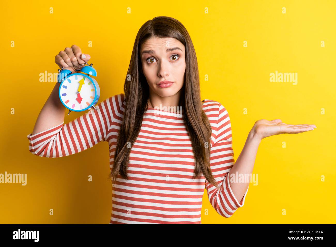 Ritratto di attraente puzzle ragazza senza cluster tenuta orologio spalle shrugging isolato su sfondo giallo brillante Foto Stock