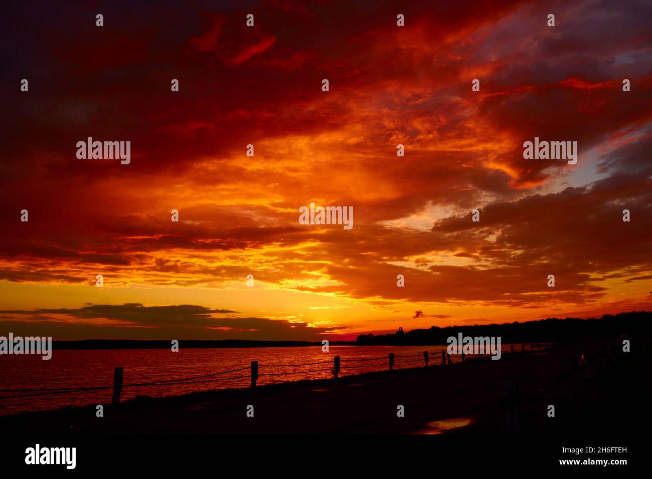 Cielo sanguinoso sopra il ponte e onde superficiali riflettenti dell'acqua. Rosso tramonto nuvoloso sopra il lago al crepuscolo. Nuvolosità serale al crepuscolo. Cielo ruddy orizzonte Foto Stock