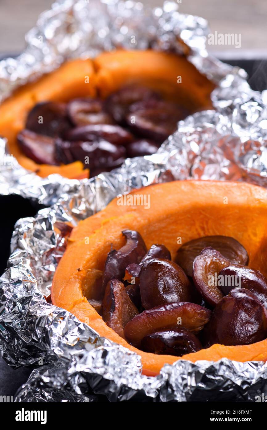 Metà della zucca di Hokkaido cotta in un foglio di alluminio farcito con prugne su un foglio da forno. Cibo vegetariano. La dieta chetogenica. Paleo vegano Foto Stock