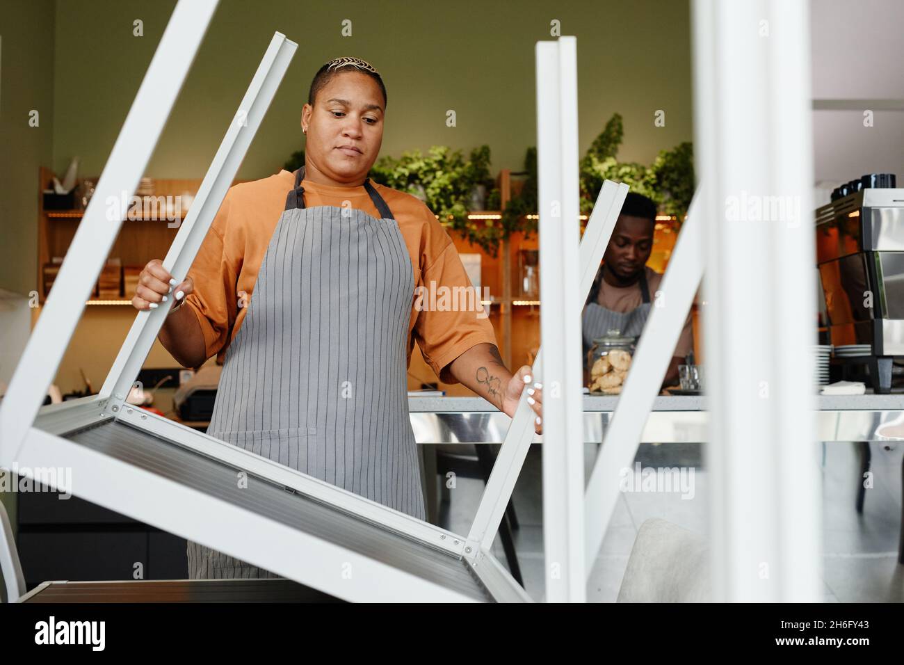 Giovane adulto afroamericano uomo e donna che inizia la giornata lavorativa in un moderno caffè preparando tavoli e spazio di lavoro Foto Stock